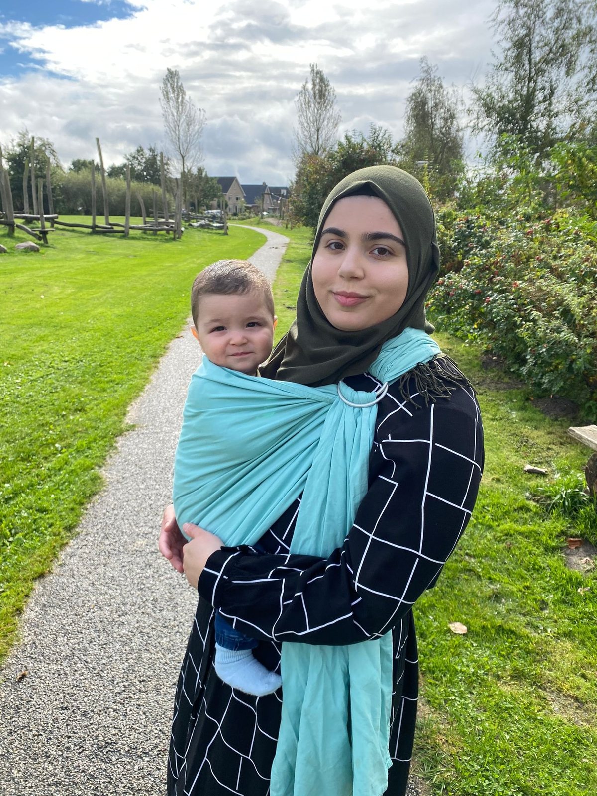 Feride draagt haar zoontje in een turquoise ringsling op een wandelpad