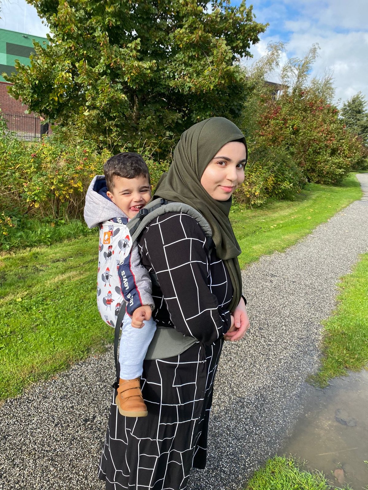 Feride draagt haar lachende peuter op de rug in een Tula peuterdrager