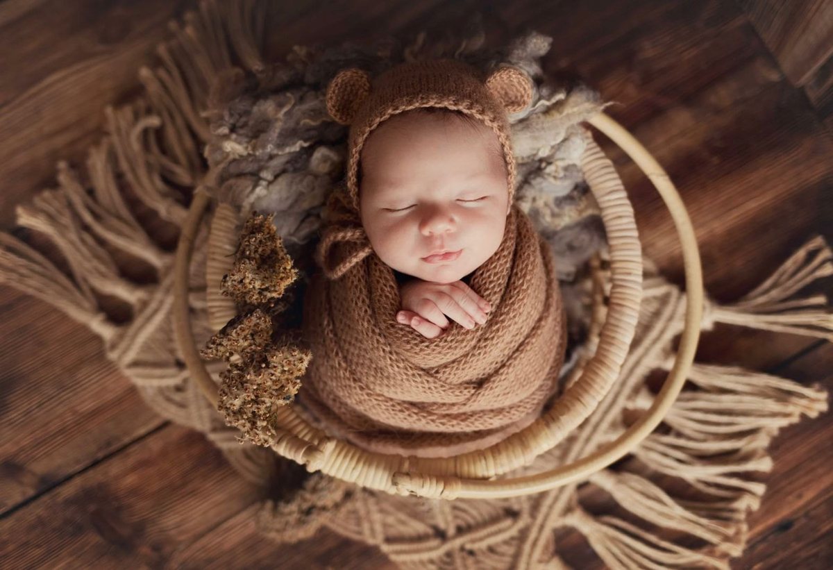 Slapende pasgeboren baby in een gebreid mutsje, gewikkeld in karamelkleurige wol in een rieten mandje
